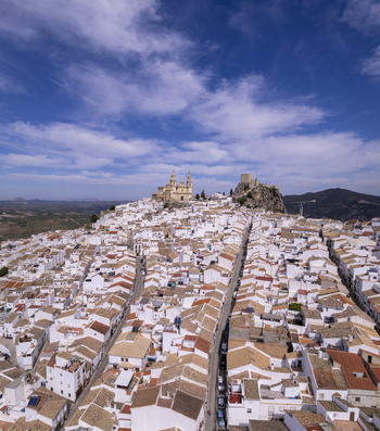 Aerial view of the historic white washed town of Olvera featuring the Church of Nuestra Senora de la Encarnacion and the hilltop castle surrounded by rolling hills in Olvera Andalusia Spain. Aerial view of the historic white washed town of Olvera featuring the Church of Nuestra Senora de la Encarnacion and the hilltop castle surrounded by rolling hills in Olvera Andalusia Spain.