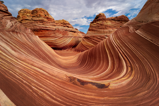 View of The Wave sandstone rock formation with undulating patterns and vibrant red and orange layers under a cloudy sky in Kanab Arizona United States. View of The Wave sandstone rock formation with undulating patterns and vibrant red and orange layers under a cloudy sky in Kanab Arizona United States.