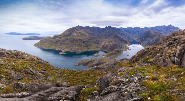 View of Sgurr na Stri overlooking the dark waters of Loch Coruisk with rugged rocky terrain and distant mountains under a cloudy sky in Isle of Skye Scotland United Kingdom. View of Sgurr na Stri overlooking the dark waters of Loch Coruisk with rugged rocky terrain and distant mountains under a cloudy sky in Isle of Skye Scotland United Kingdom.