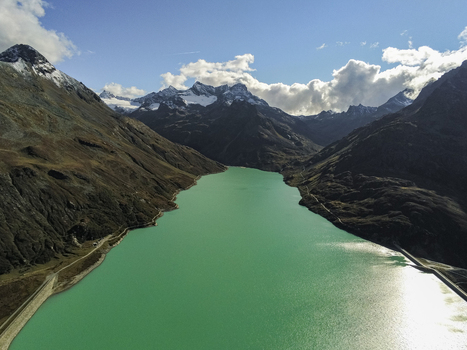 Aerial view of a turquoise reservoir surrounded by rugged alpine mountains with snow capped peaks and rocky slopes under a bright sky Austria. Aerial view of a turquoise reservoir surrounded by rugged alpine mountains with snow capped peaks and rocky slopes under a bright sky Austria.