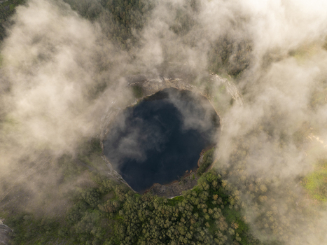 Aerial view of the volcanic crater lake in Kelimutu National Park surrounded by lush forest and drifting clouds in Detusoko East Nusa Tenggara Indonesia.
