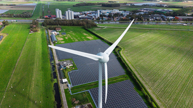 Aerial view of a wind turbine and a large solar panel array situated in green fields near a canal and industrial buildings in t Zand North Holland Netherlands. Aerial view of a wind turbine and a large solar panel array situated in green fields near a canal and industrial buildings in t Zand North Holland Netherlands.