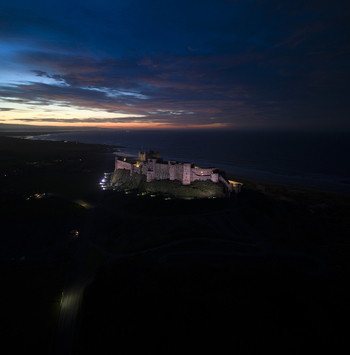 Aerial view of Bamburgh Castle illuminated on a rocky outcrop overlooking the North Sea under a twilight sky Bamburgh England United Kingdom. Aerial view of Bamburgh Castle illuminated on a rocky outcrop overlooking the North Sea under a twilight sky Bamburgh England United Kingdom.