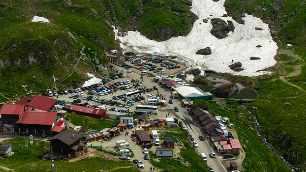 Aerial view of the Transfagarasan mountain pass featuring a busy parking area with vehicles small shops and patches of snow on the green slopes in Curtea de Arges Judetul Arges Romania.