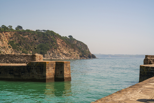 View of the historic stone harbour walls and calm turquoise water at the coast in Charlestown Cornwall United Kingdom. View of the historic stone harbour walls and calm turquoise water at the coast in Charlestown Cornwall United Kingdom.