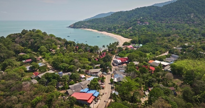 Aerial view of a coastal town with lush green hills a sandy beach turquoise waters and small buildings nestled among trees in Phuket Phuket Thailand. Aerial view of a coastal town with lush green hills a sandy beach turquoise waters and small buildings nestled among trees in Phuket Phuket Thailand.