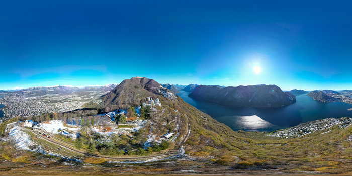 Aerial view of Lake Lugano surrounded by snow dusted mountains and the city skyline under a clear blue sky in Lugano Ticino Switzerland.