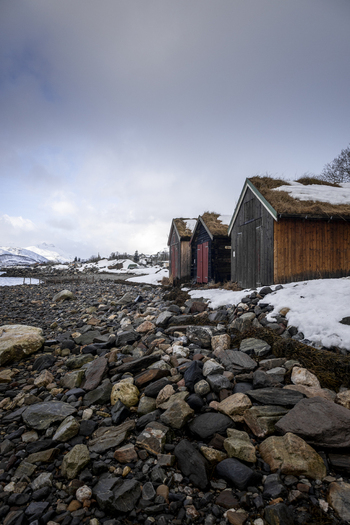 View of traditional wooden cabins with sod roofs on a rocky shoreline with snow and distant mountains in Kvaloya Troms Norway. View of traditional wooden cabins with sod roofs on a rocky shoreline with snow and distant mountains in Kvaloya Troms Norway.