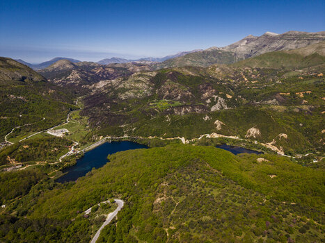 Aerial view of the Blue Eye spring surrounded by lush green hills winding roads and mountainous terrain in Finiq Vlore County Albania. Aerial view of the Blue Eye spring surrounded by lush green hills winding roads and mountainous terrain in Finiq Vlore County Albania.