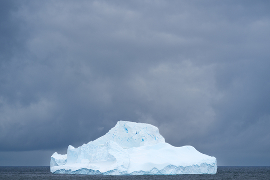 View of an iceberg floating in the ocean under a dark cloudy sky in the South Orkney Islands. View of an iceberg floating in the ocean under a dark cloudy sky in the South Orkney Islands.