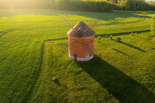Aerial view of a historic brick windmill surrounded by vibrant green fields and long shadows during golden hour in Chvalkovice Hradec Kralove Region Czechia.