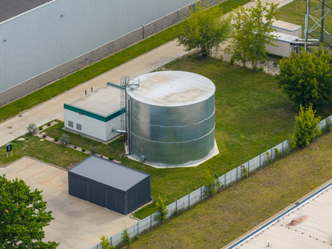 Aerial view of a large cylindrical metal water tank for fire safety systems situated in an industrial area with green grass and nearby buildings in Warsaw Mazowieckie Poland. Aerial view of a large cylindrical metal water tank for fire safety systems situated in an industrial area with green grass and nearby buildings in Warsaw Mazowieckie Poland.