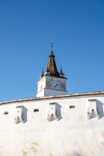 View of the historic clock tower of the Prejmer Fortified Church rising above white defensive walls against a clear blue sky in Prejmer Brasov Romania. View of the historic clock tower of the Prejmer Fortified Church rising above white defensive walls against a clear blue sky in Prejmer Brasov Romania.