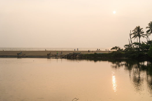 View of traditional outrigger boats and people on a sandy beach by calm water at sunset Galle Southern Province Sri Lanka.