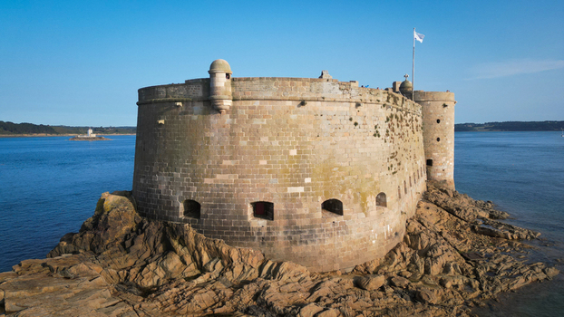 Aerial view of a stone fortress standing proudly on a rocky outcrop surrounded by the turquoise sea its weathered walls a testament to time Plouezoc h Bretagne France.