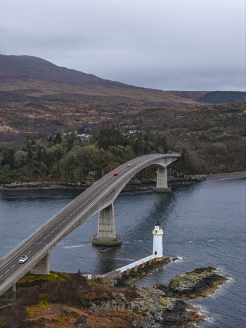Aerial view of Skye Bridge and Kyleakin Lighthouse over the sea with rugged hills under an overcast sky Isle of Skye Scotland United Kingdom.