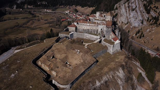 Aerial view of the historic Chateau de Joux fortress perched on a rocky hill surrounded by mountain slopes and a valley in La Cluse et Mijoux Bourgogne Franche Comte France. Aerial view of the historic Chateau de Joux fortress perched on a rocky hill surrounded by mountain slopes and a valley in La Cluse et Mijoux Bourgogne Franche Comte France.