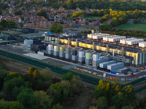 Aerial view of a modern data center facility with rooftop cooling units and industrial infrastructure surrounded by trees and residential buildings in the United Kingdom. Aerial view of a modern data center facility with rooftop cooling units and industrial infrastructure surrounded by trees and residential buildings in the United Kingdom.