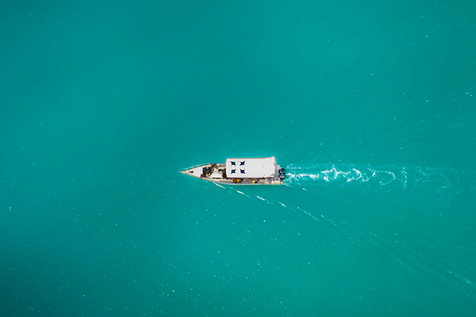 Aerial view of a small white boat moving through vibrant turquoise water in Indonesia. Aerial view of a small white boat moving through vibrant turquoise water in Indonesia.