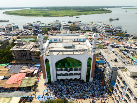 Aerial view of a grand mosque with striking white walls and green accents surrounded by bustling markets and waterways Charmonai Barisal Division Bangladesh. Aerial view of a grand mosque with striking white walls and green accents surrounded by bustling markets and waterways Charmonai Barisal Division Bangladesh.