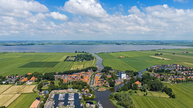 Aerial view of the historic town of Sloten with its canal marina and surrounding green farmland set against a large lake under a bright blue sky in Sloten Friesland Netherlands.