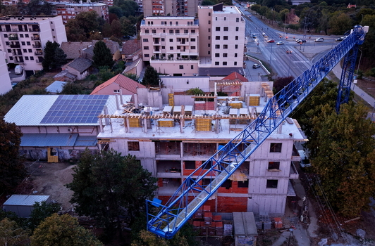 Aerial view of a construction site featuring a large blue crane and a concrete building structure with solar panels on the adjacent roof in Pancevo Vojvodina Serbia.