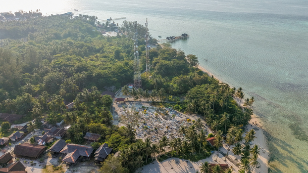 Aerial view of Pulau Derawan cemetery surrounded by lush palm trees and communication towers near the turquoise coastline in Pulau Derawan East Kalimantan Indonesia. Aerial view of Pulau Derawan cemetery surrounded by lush palm trees and communication towers near the turquoise coastline in Pulau Derawan East Kalimantan Indonesia.