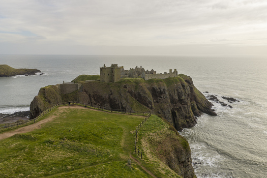 Aerial view of Dunnottar Castle perched on dramatic cliffs overlooking the North Sea with green fields in the foreground Stonehaven Scotland United Kingdom. Aerial view of Dunnottar Castle perched on dramatic cliffs overlooking the North Sea with green fields in the foreground Stonehaven Scotland United Kingdom.