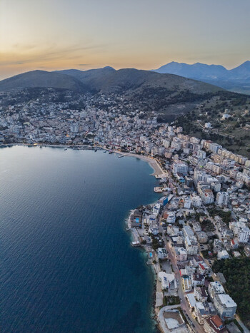 Aerial view of the coastal city of Saranda with its dense urban buildings waterfront promenade and hills overlooking the Ionian Sea at sunset in Saranda Vlore County Albania. Aerial view of the coastal city of Saranda with its dense urban buildings waterfront promenade and hills overlooking the Ionian Sea at sunset in Saranda Vlore County Albania.