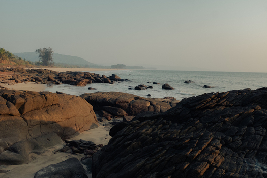 View of golden light kissing the rugged dark rocks on the shore as the sea meets the sandy beach under a hazy sky Chiplun Maharashtra India. View of golden light kissing the rugged dark rocks on the shore as the sea meets the sandy beach under a hazy sky Chiplun Maharashtra India.
