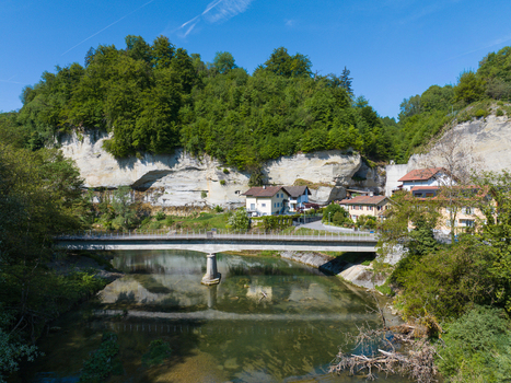 Aerial view of the Pont de la Motta bridge spanning the Sarine river with limestone cliffs traditional houses and lush green forest under a clear blue sky in Fribourg Fribourg Switzerland. Aerial view of the Pont de la Motta bridge spanning the Sarine river with limestone cliffs traditional houses and lush green forest under a clear blue sky in Fribourg Fribourg Switzerland.