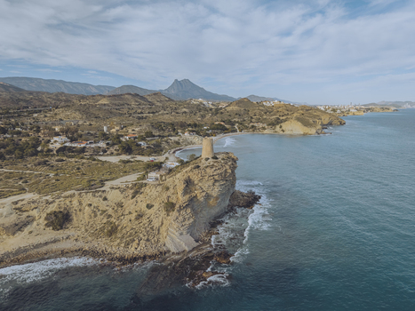 Aerial view of Torre del Xarco on a rocky cliff overlooking the turquoise sea with mountains in the background La Vila Joiosa Comunidad Valenciana Spain.