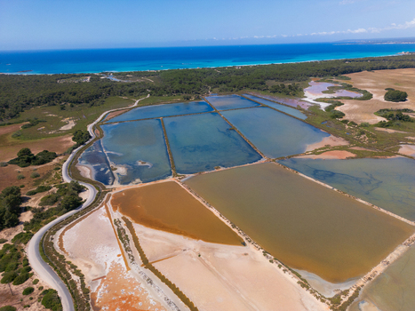 Aerial view of Salines des Trenc salt evaporation ponds with multi colored basins near the turquoise sea and coastal vegetation in Campos Islas Baleares Spain. Aerial view of Salines des Trenc salt evaporation ponds with multi colored basins near the turquoise sea and coastal vegetation in Campos Islas Baleares Spain.