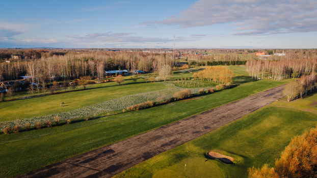 Valmiera Latvija 18 November 2025 Aerial view of a golf club building and course on a frosty morning with green fairways scattered trees and a clear sky.