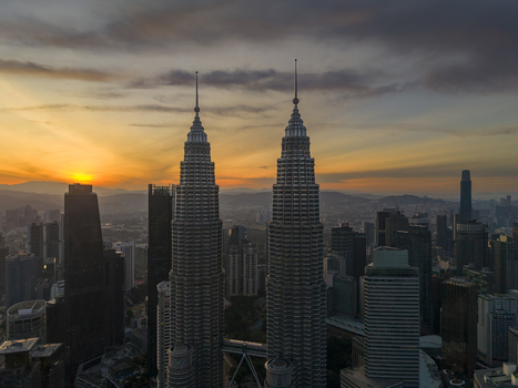 Kuala Lumpur Malaysia 11 March 2026 Aerial view of the Petronas Twin Towers glowing against a vibrant sunset sky with the city skyline and distant mountains.