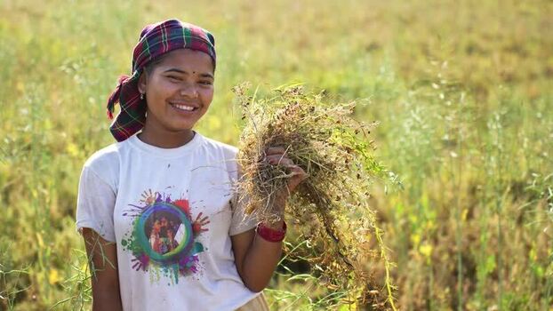 View of a smiling woman holding harvested crops in a field Nepal.