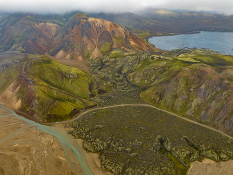 Aerial view of a serpentine river snaking through a rugged landscape of moss covered lava fields and colorful mountains under a cloudy sky Highlands Iceland.