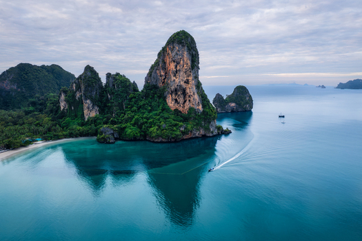 Aerial view of Railay Beach with dramatic limestone cliffs rising from turquoise waters a small boat leaving a wake and lush greenery in Ao Nang Krabi Thailand. Aerial view of Railay Beach with dramatic limestone cliffs rising from turquoise waters a small boat leaving a wake and lush greenery in Ao Nang Krabi Thailand.