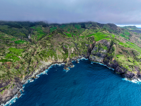 Aerial view of where the dramatic cliffs meet the deep blue sea under a sky heavy with brooding clouds Faj&atilde; Grande Azores Portugal.