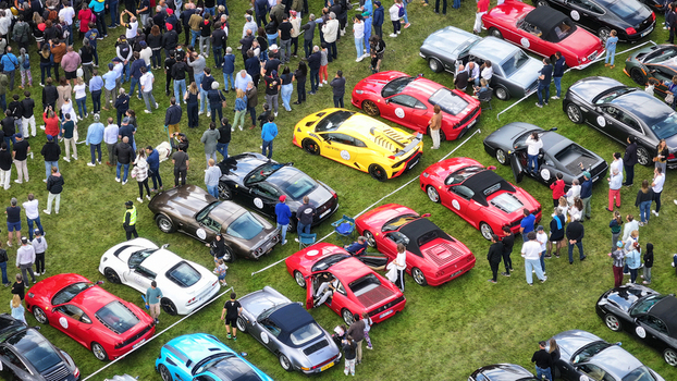 La Chapelle de Guinchay France 01 June 2024 Aerial view of a luxury sports car exhibition on a green lawn with a large crowd of people admiring rows of colorful Ferraris and Porsches. La Chapelle de Guinchay France 01 June 2024 Aerial view of a luxury sports car exhibition on a green lawn with a large crowd of people admiring rows of colorful Ferraris and Porsches.