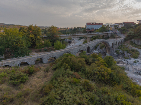 Aerial view of the historic Mesi Bridge with its stone arches spanning a dry riverbed surrounded by lush greenery and trees in Boks Qarku i Shkodres Albania.