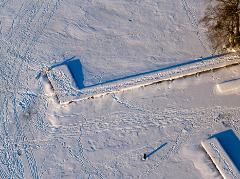 Aerial view of a snow covered wooden pier on a frozen lake with numerous footprints and long shadows in Trakai Vilnius County Lithuania. Aerial view of a snow covered wooden pier on a frozen lake with numerous footprints and long shadows in Trakai Vilnius County Lithuania.