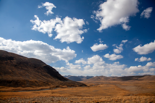 View of the vast golden plateau of Deosai National Park with rolling hills under a bright blue sky with scattered white clouds in Astore Gilgit Pakistan. View of the vast golden plateau of Deosai National Park with rolling hills under a bright blue sky with scattered white clouds in Astore Gilgit Pakistan.
