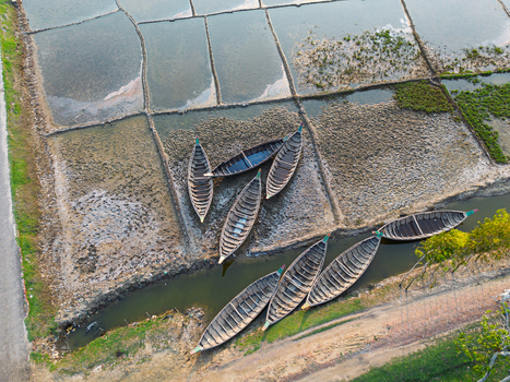 Aerial view of traditional wooden boats resting in a narrow canal and on dry salt pans under soft daylight in Moheskhali Upazila Chittagong Division Bangladesh. Aerial view of traditional wooden boats resting in a narrow canal and on dry salt pans under soft daylight in Moheskhali Upazila Chittagong Division Bangladesh.