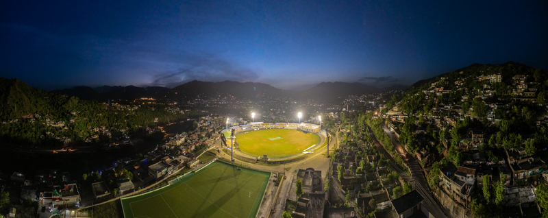 Aerial view of the illuminated Muzaffarabad Cricket Stadium at twilight surrounded by city lights and dark mountain peaks in Muzaffarabad Azad Kashmir Pakistan. Aerial view of the illuminated Muzaffarabad Cricket Stadium at twilight surrounded by city lights and dark mountain peaks in Muzaffarabad Azad Kashmir Pakistan.