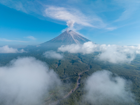Aerial view of Mount Semeru with a volcanic smoke plume rising above lush green forests and scattered clouds in Pronojiwo East Java Indonesia. Aerial view of Mount Semeru with a volcanic smoke plume rising above lush green forests and scattered clouds in Pronojiwo East Java Indonesia.