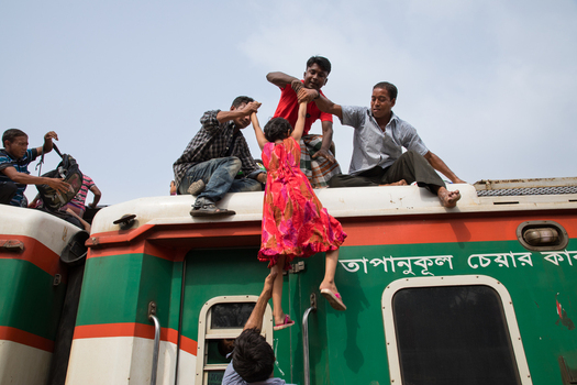 Dhaka Bangladesh 14 June 2018 View of men helping a young girl in a pink dress climb onto the roof of a crowded train at Airport Railway Station during the Eid holiday rush. Dhaka Bangladesh 14 June 2018 View of men helping a young girl in a pink dress climb onto the roof of a crowded train at Airport Railway Station during the Eid holiday rush.