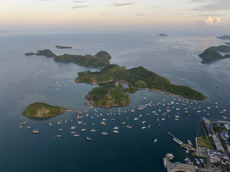 Aerial view of Labuan Bajo harbor filled with numerous boats and ships surrounded by lush green islands at sunset in Komodo East Nusa Tenggara Indonesia. Aerial view of Labuan Bajo harbor filled with numerous boats and ships surrounded by lush green islands at sunset in Komodo East Nusa Tenggara Indonesia.
