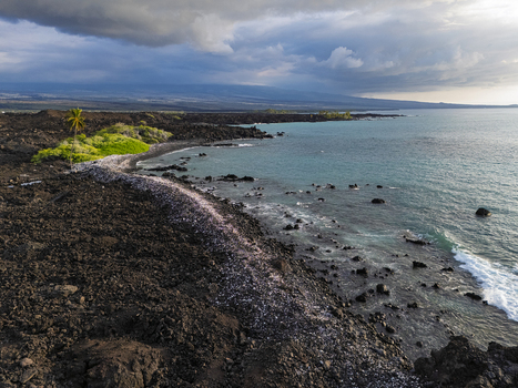 Aerial view of the rugged black lava rock coastline and turquoise ocean waves at Waikoloa Beach under a cloudy sky in Waikoloa Village Hawaii United States.