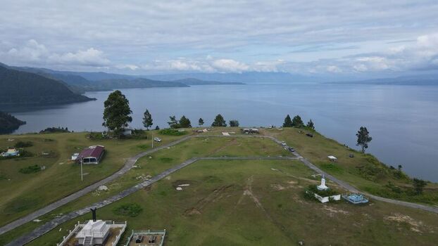 Aerial view of Tara Bunga overlooking the vast expanse of Lake Toba with grassy hills winding paths and scattered trees in Tampahan North Sumatra Indonesia. Aerial view of Tara Bunga overlooking the vast expanse of Lake Toba with grassy hills winding paths and scattered trees in Tampahan North Sumatra Indonesia.